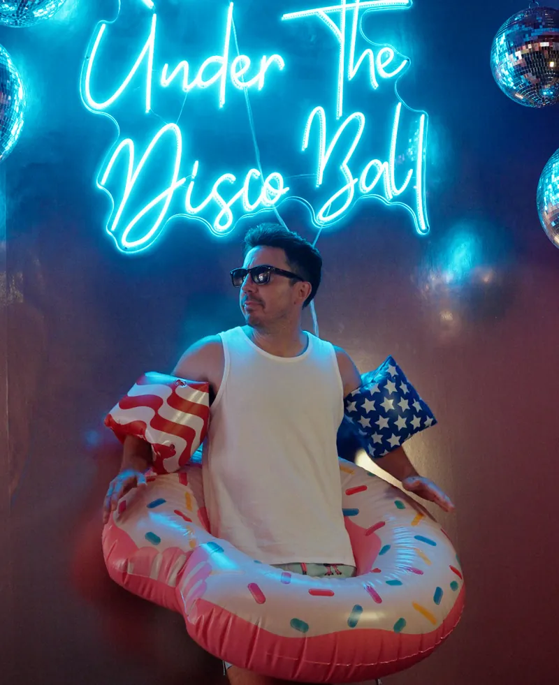 Evan Lopez in a pool float under a neon sign